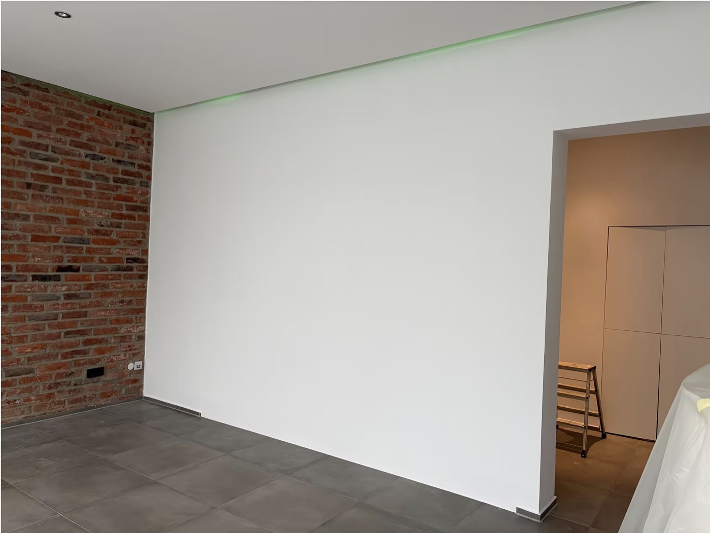 Neu verputzte Wand mit indirekter Beleuchtung neben Sichtmauerwerk